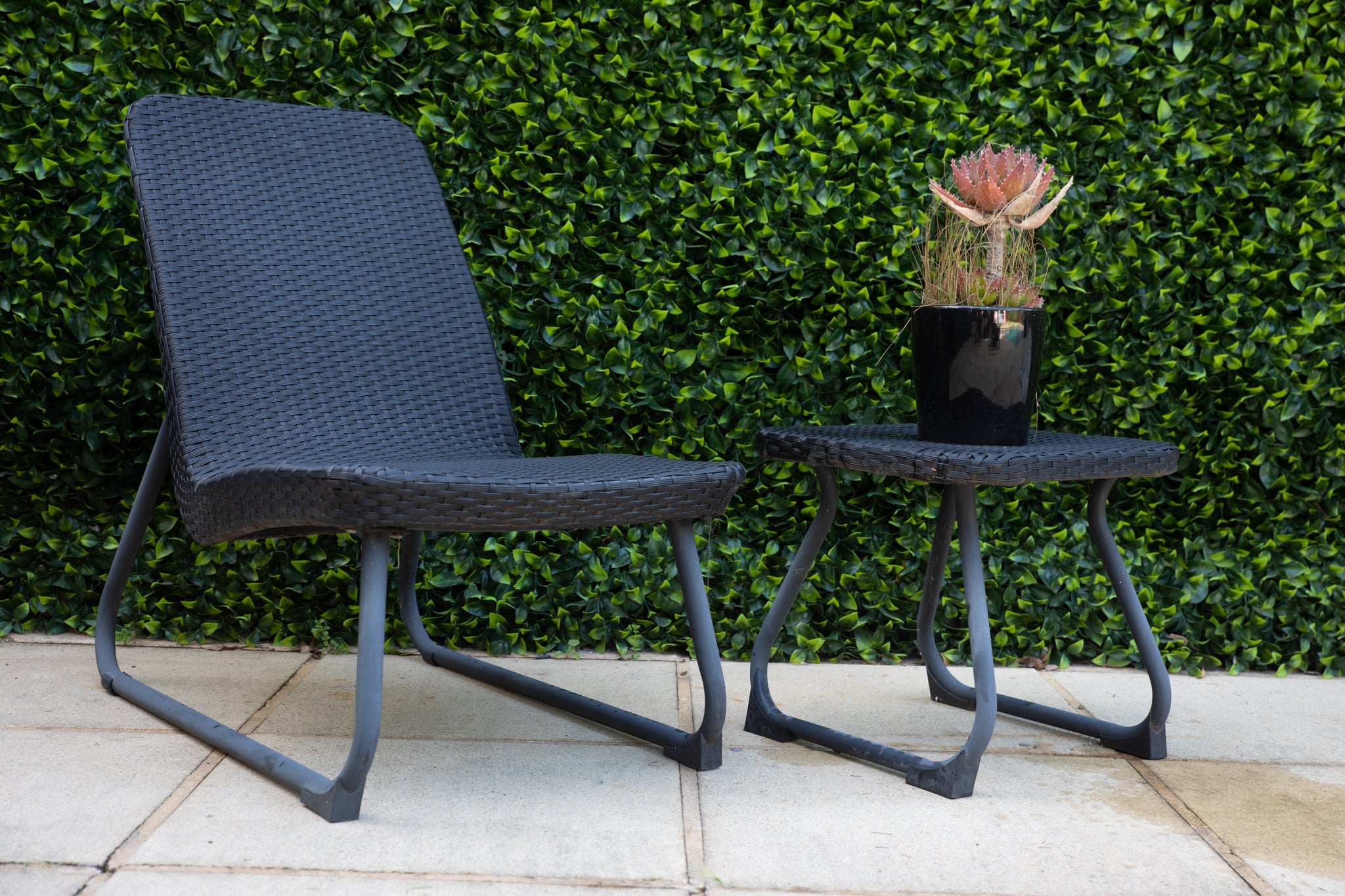 An outdoor chair placed in front of a lush, artificial green wall