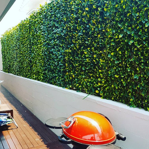 Side view of an outdoor artificial green wall extending along a white concrete retaining wall.